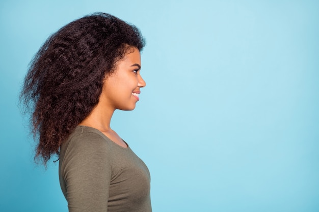 Foto lateral de perfil de una chica afroamericana alegre positiva tiene tiempo libre con sus amigos, mira el espacio de la copia, escucha, disfruta de las vacaciones, usa un jersey elegante aislado sobre una pared de color azul