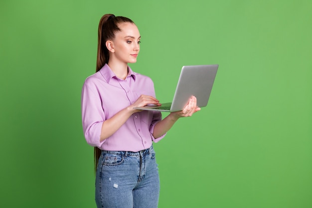 Foto lateral de perfil de una chica trabajadora ceo centrada mentalmente que trabaja con una computadora portátil remota que tiene una comunicación por wifi de redes sociales vistiendo violeta lila aislado sobre fondo de color verde