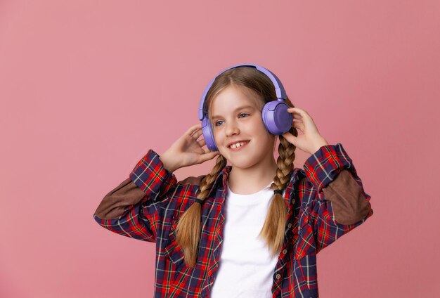 Foto de una linda y graciosa adolescente con auriculares saltadores rosas bailando disfrutando de la música en un fondo