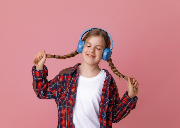 Foto de una linda y graciosa adolescente con auriculares saltadores rosas bailando disfrutando de la música en un fondo