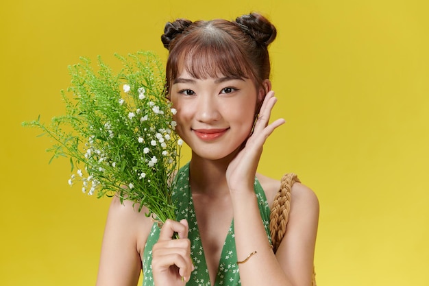 Foto de una linda joven asiática sosteniendo flores usando ropa de verano aislada en un fondo amarillo