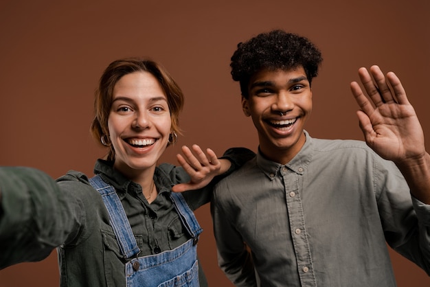 Foto de una linda pareja de agricultores toma un selfie con una bonita sonrisa. La mujer viste overoles de mezclilla, el hombre viste camiseta, fondo de color marrón aislado.