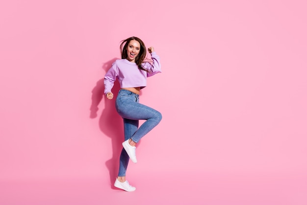 Foto de longitud completa de la niña encantada celebrar la lotería ganar levantar puños gritar sí usar zapatillas lila pullover aisladas sobre fondo de color pastel