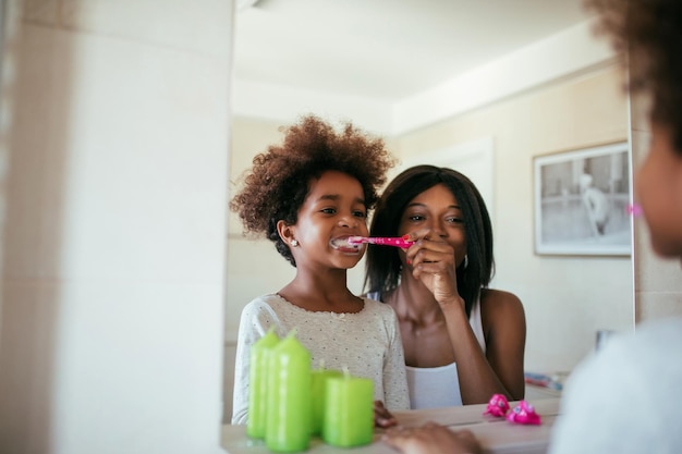 Foto de madre afroamericana e hija cepillándose los dientes por la mañana