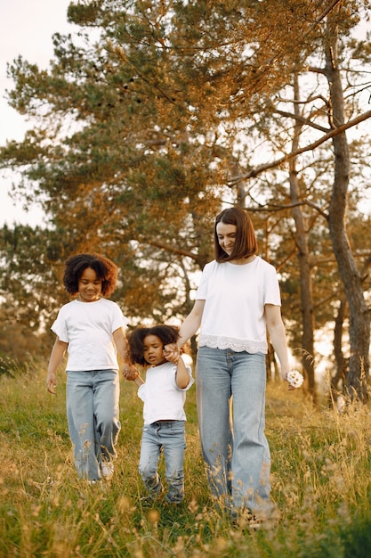 Foto de madre caucásica y sus dos hijas afroamericanas caminando juntos al aire libre. Las niñas y la madre cogidos de la mano