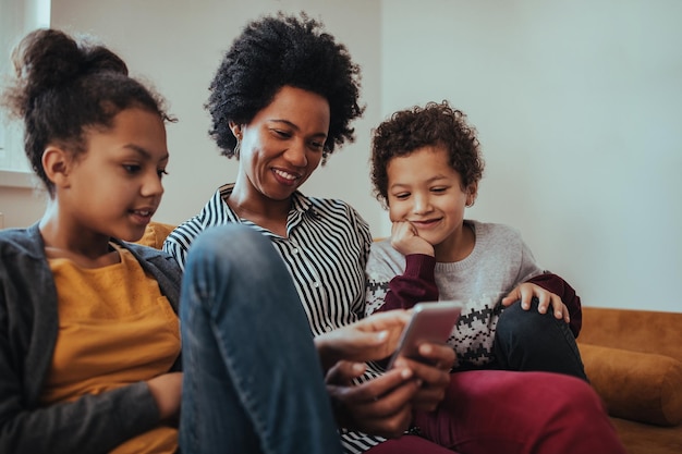 Foto de una madre sentada en el sofá con sus hijos mirando el teléfono móvil