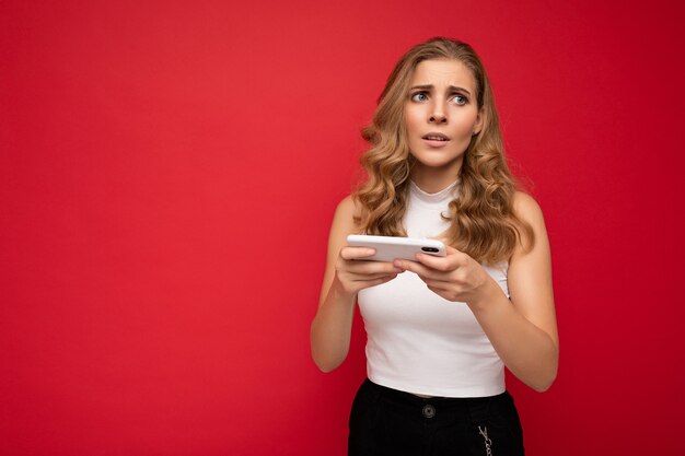 Foto de malestar joven y bella mujer rubia vistiendo camiseta blanca aislado sobre fondo rojo con