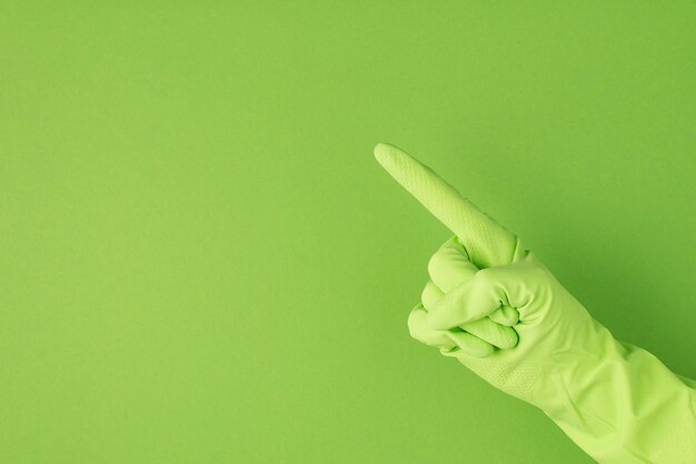 Foto foto de mano en guante de goma verde haciendo símbolo señalador con el dedo índice sobre fondo verde aislado con copyspace