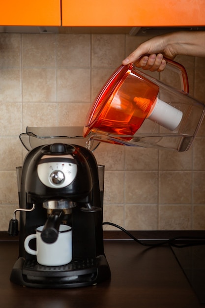 Foto de la mano del hombre vertiendo agua de una jarra en una cafetera en la cocina