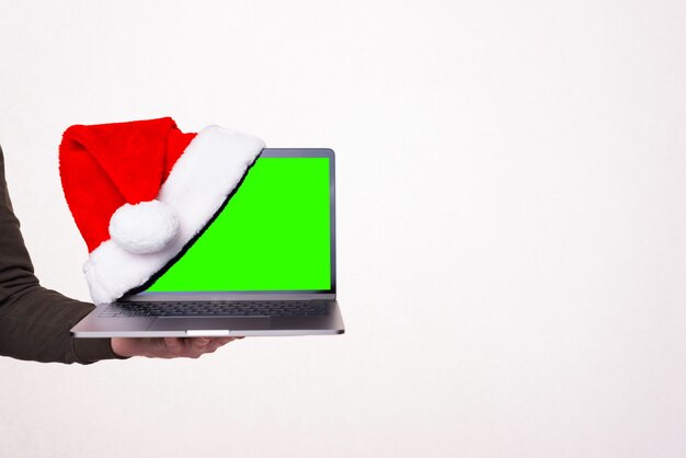 Foto de mano sujetando portátil con sombrero rojo, concepto de descuentos de vacaciones de navidad