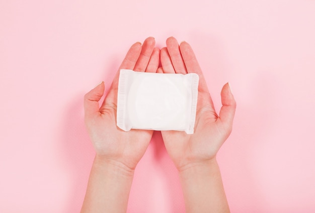 Foto de manos femeninas sosteniendo una toalla sanitaria en rosa