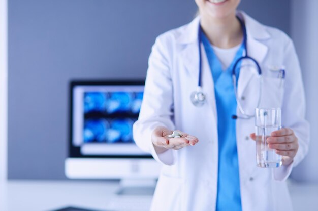 Una foto de las manos del médico sosteniendo pastillas y un vaso de agua en la clínica