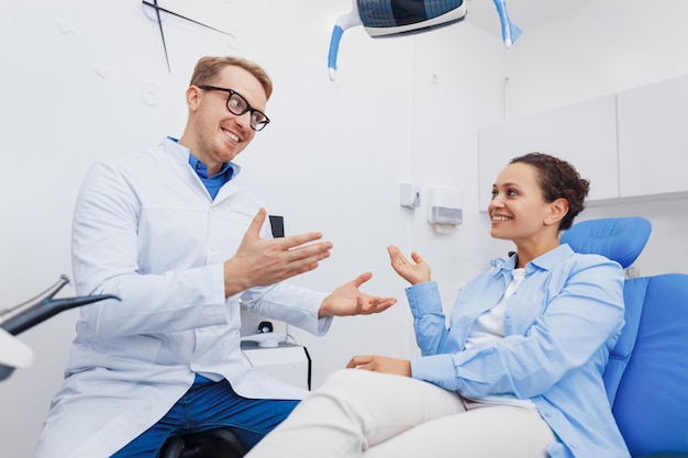 Foto de un médico dental amigable hablando con un paciente sonriente en una silla dental sobre tratamiento médico