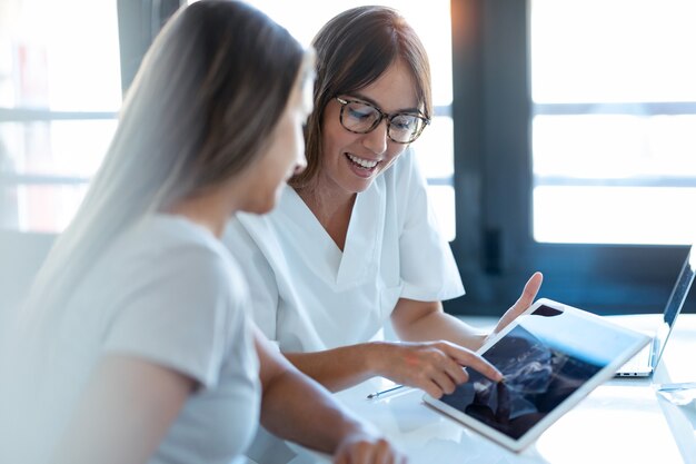 Foto de médico ginecólogo joven mostrando al bebé de ecografía de mujer embarazada con tableta digital en consulta médica.