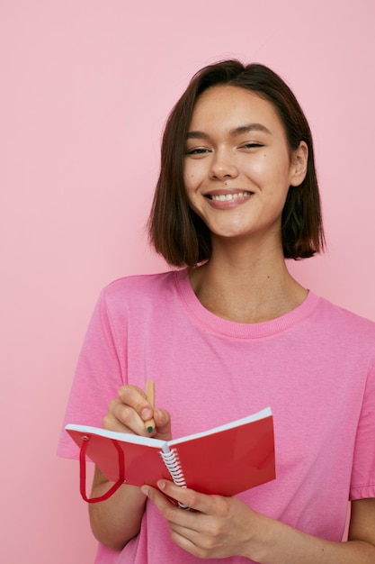 Foto menina bonita em um caderno vermelho de camiseta rosa e fundo rosa de caneta