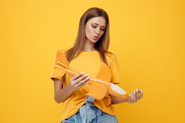 Foto menina bonita posando avião amarelo nas mãos de fundo amarelo divertido