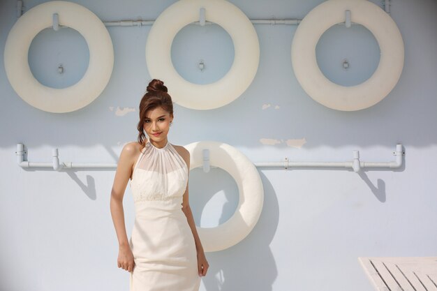 Foto minimalista, garota fashion em coisas elegantes de verão - camisa branca. Retrato da noiva bonita no vestido de casamento contra o círculo branco da vida em uma parede azul brilhante.