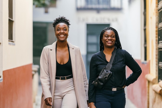 Foto mit selektivem Fokus auf zwei lächelnde afrikanische weibliche Models, die in einer engen Straße spazieren gehen