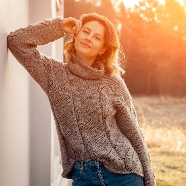 Foto de moda al aire libre de una mujer joven y hermosa con suéter de punto marrón y jeans en un paisaje de campo otoñal Lookbook de moda
