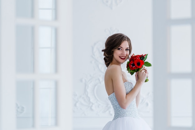 Foto de moda de una bella novia con ramo de flores en sus manos en la sala de luz al lado de las puertas