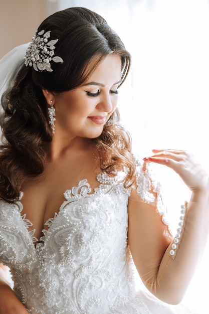 Foto foto de moda de una hermosa novia con cabello oscuro en un elegante vestido de novia y un impresionante maquillaje en la habitación en la mañana de la boda la novia se está preparando para la boda