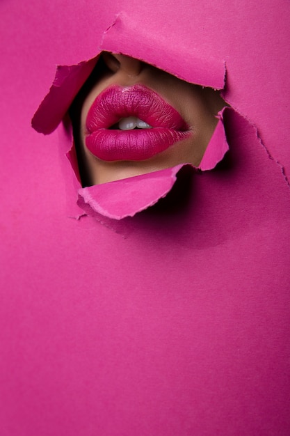Foto de moda Hermosos labios rojos, lápiz labial y brillo de labios sobresalen del agujero del papel rosa