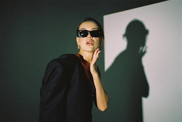 Una foto de moda moderna tomada con una cámara de cine Una modelo femenina con gafas de sol posa en el estudio sobre un fondo blanco