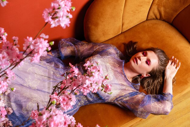 Foto de moda de mujer joven hermosa en vestido hermoso con flores posando acostado en el sofá fas ...