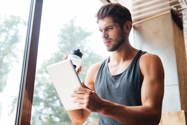 Foto de modelo en gimnasio con tableta y botella