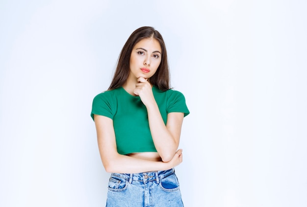 Foto de un modelo de niña pensativa de pie y posando contra la pared blanca.