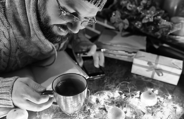 Foto monocroma de hombre con un libro en blanco en sus manos para la mesa de año nuevo con decoraciones