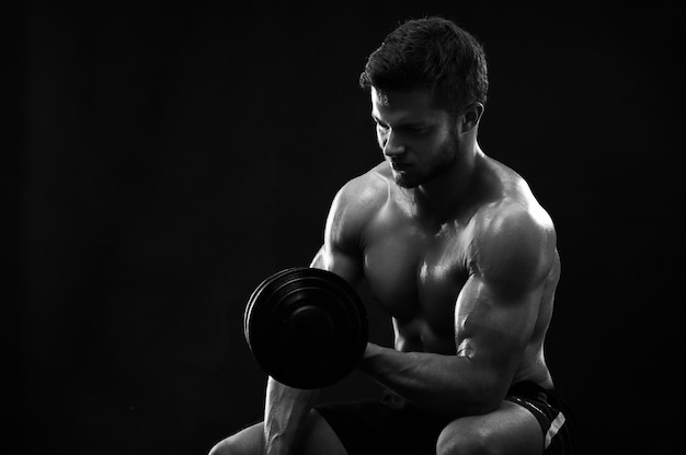 Foto monocroma de un joven deportista rasgado atlético con dumbb