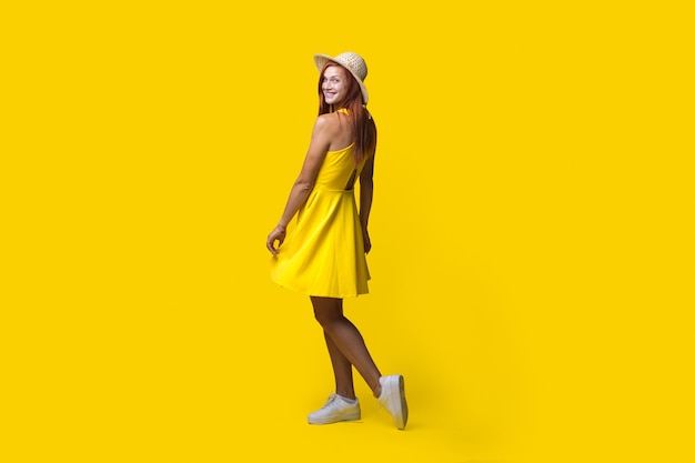 Foto monocroma de una mujer pelirroja posando con un vestido con sombrero en una pared amarilla del estudio