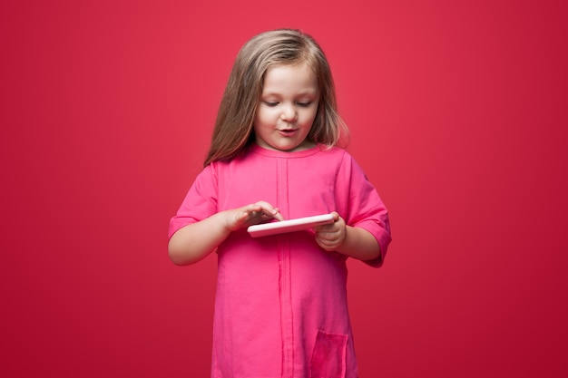 Foto monocroma de un niño caucásico con cabello rubio jugando con un juguete en una pared roja del estudio con un vestido de verano