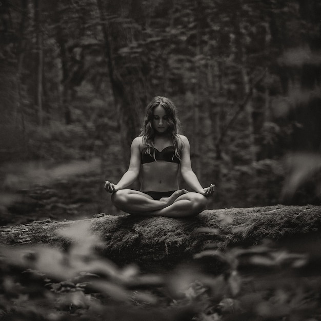 Foto monocromática de mulher europeia sentada na floresta sozinha e meditando