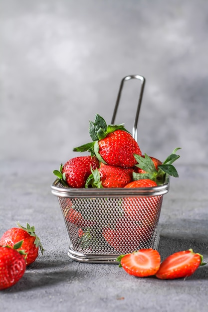 Foto del montón de fresas frescas en la cesta en fondo gris rústico. Un montón de fresas maduras en una cesta de acero sobre la mesa. Copia espacio Fruta fresca y saludable. Alimentos orgánicos. Comida clara