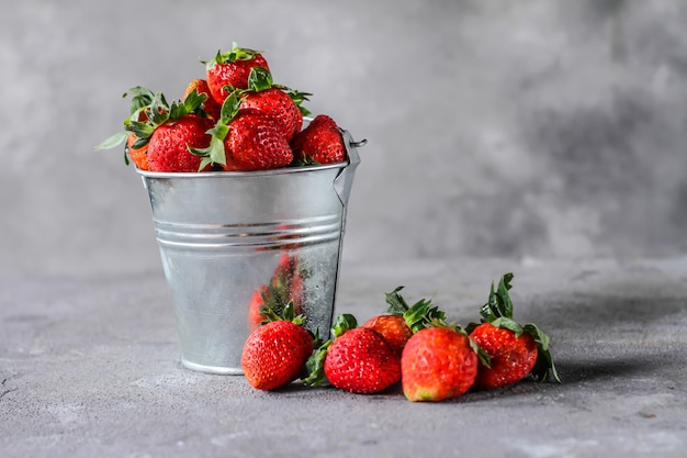 Foto del montón de fresas frescas en el tazón de fuente en fondo gris rústico. Un montón de fresas maduras en un recipiente de lata sobre la mesa. Copia espacio Fruta fresca y saludable. Alimentos orgánicos. Comida clara