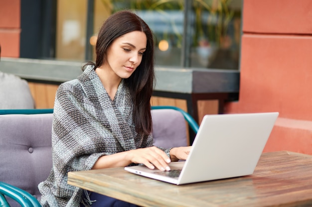Foto de una morena joven estudiante se prepara para estudiar seminario, teclados en la computadora portátil, envuelto en colcha