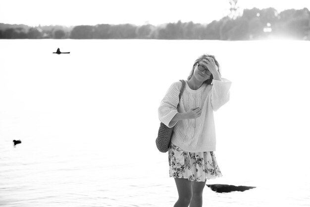 Esta foto muestra a una joven rubia caminando por la playa con un vestido y un suéter con flores en un día soleado