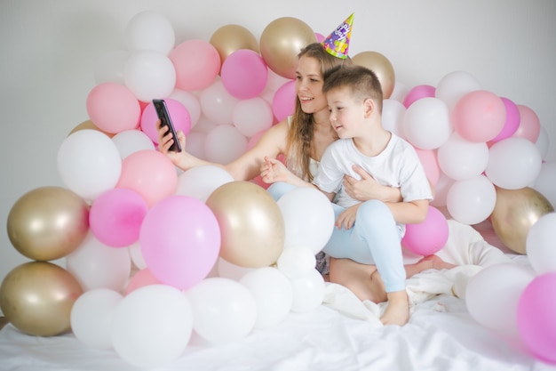 Foto de mujer alegre con niño niño sonriendo y tomando foto selfie en teléfono celular con globo