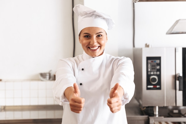 Foto de mujer atractiva chef vistiendo uniforme blanco cocinar comida, en la cocina del restaurante