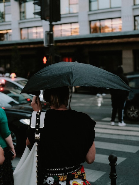 Foto foto de una mujer caminando por el cruce de peatones con un paraguas negro