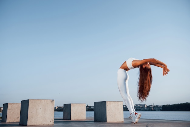 Foto de mujer deportiva haciendo ejercicios de fitness cerca del lago durante el día