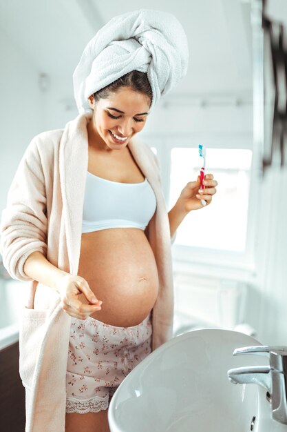 Una foto de una mujer embarazada cepillándose los dientes en el baño.