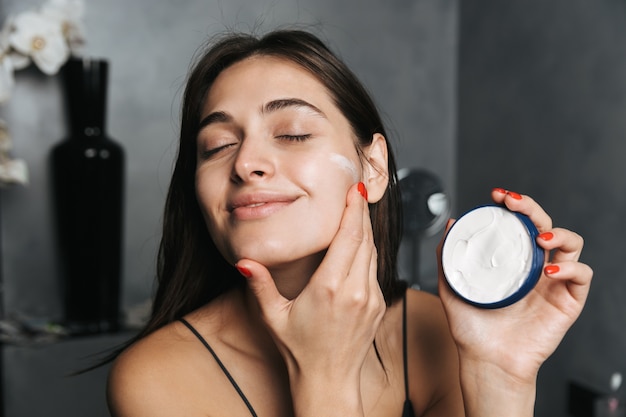 Foto de mujer feliz con largo cabello oscuro de pie en el baño.