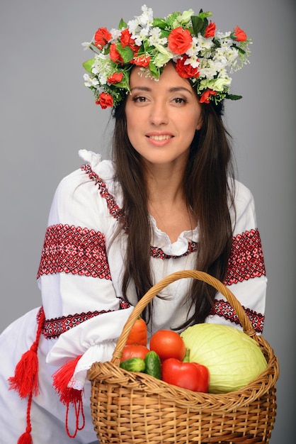 Foto de una mujer hermosa y linda en traje ucraniano con cesta de verduras