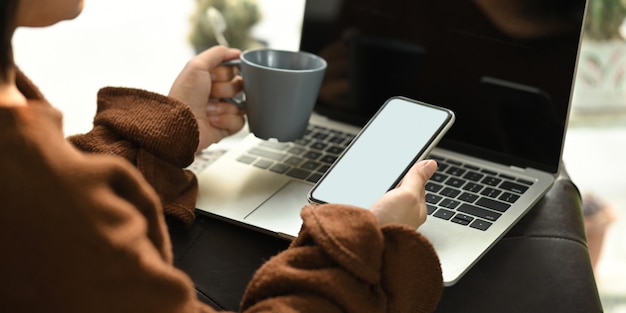 Foto de una mujer hermosa que se relaja en sus vacaciones sentándose en el sofá de cuero y tomando un café caliente mientras usa una computadora portátil con pantalla en blanco que se pone en su regazo. Mujer relajarse tiempo.