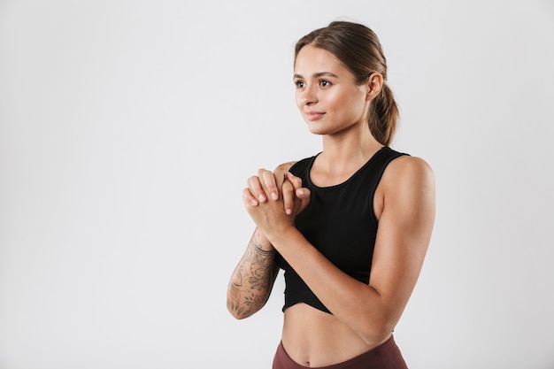 Foto de mujer hermosa en ropa deportiva estirando sus brazos mientras hace ejercicio aislado sobre pared blanca