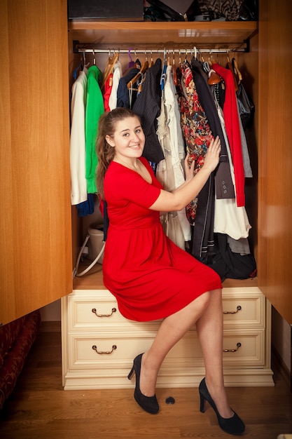 Foto de mujer hermosa en vestido rojo sentada en un gran armario