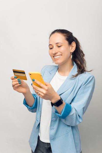 Foto de mujer joven alegre en casual haciendo una transferencia con tarjeta de crédito y smartphone